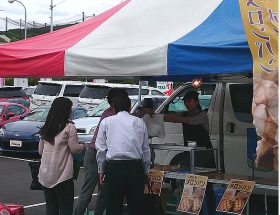 自動車販売店前でメロンパンをプレゼントする様子